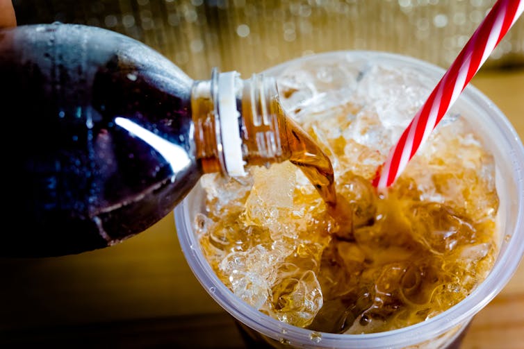 A dark bubbly liquid is poured into a cup filled with ice.