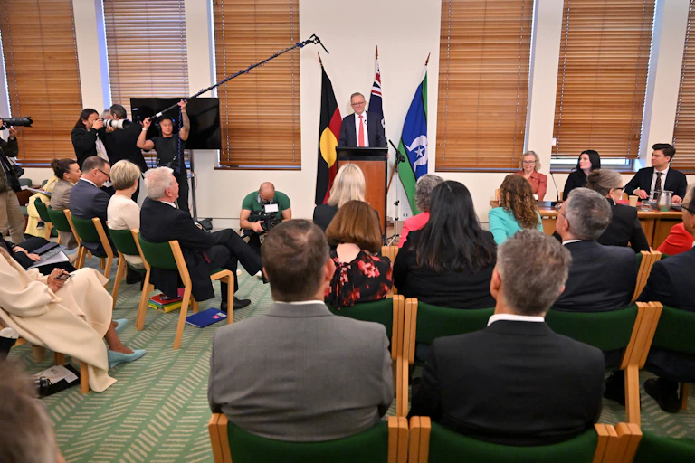 A man speaks at a lectern in front of a group of people in seats.