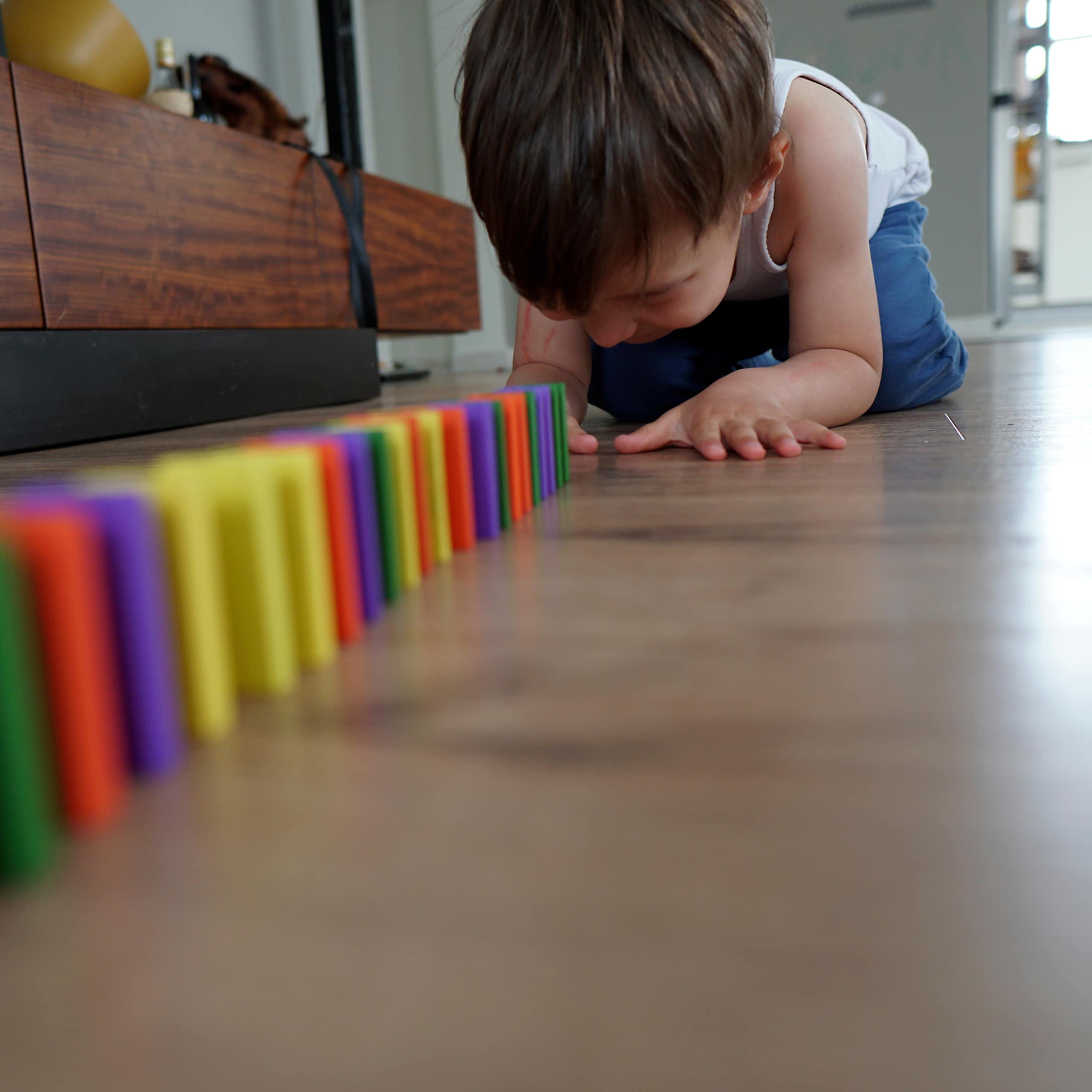 boy on living room floor sets up colourful dominoes in straight line