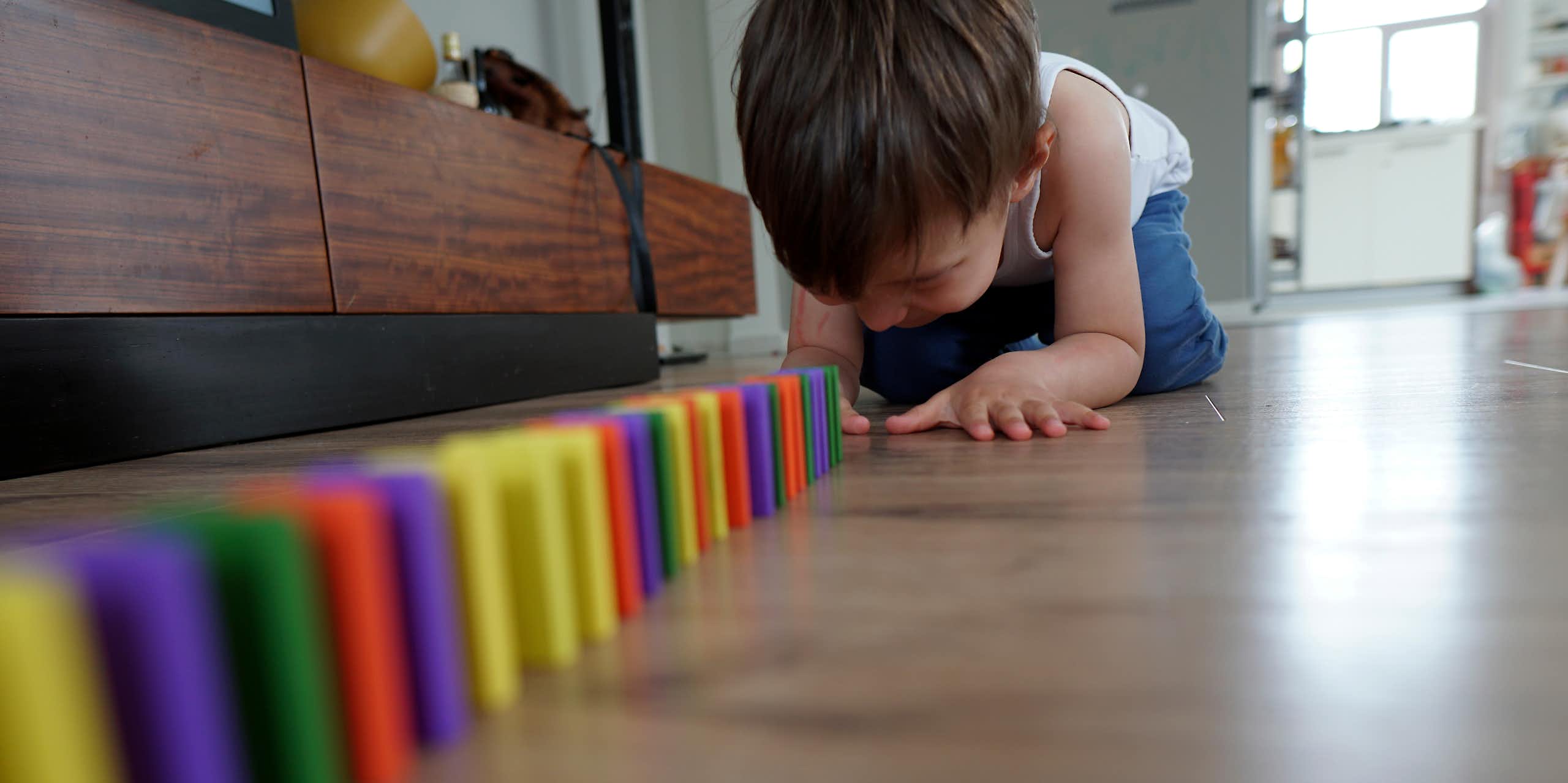 boy on living room floor sets up colourful dominoes in straight line