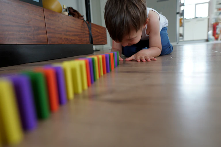 boy on living room floor sets up colourful dominoes in straight line