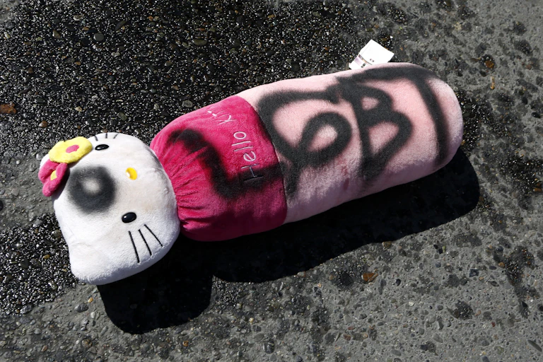 A stuffed Hello Kitty toy discarded on asphalt.