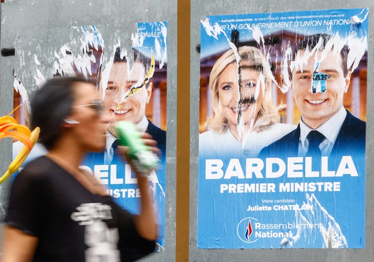 A woman walks past a damaged poster of Marine Le Pen and Jordan Bardella.