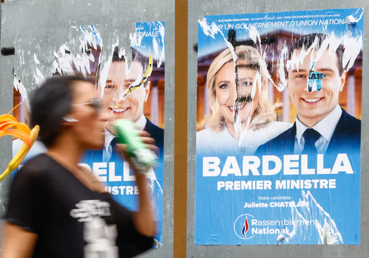 A woman walking past a damaged poster of Marine Le Pen and Jordan Bardella.