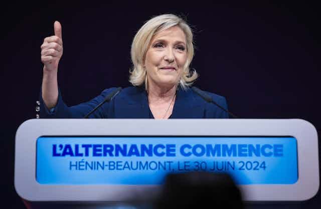 Marine Le Pen smirking and holding her thumb up in the air.