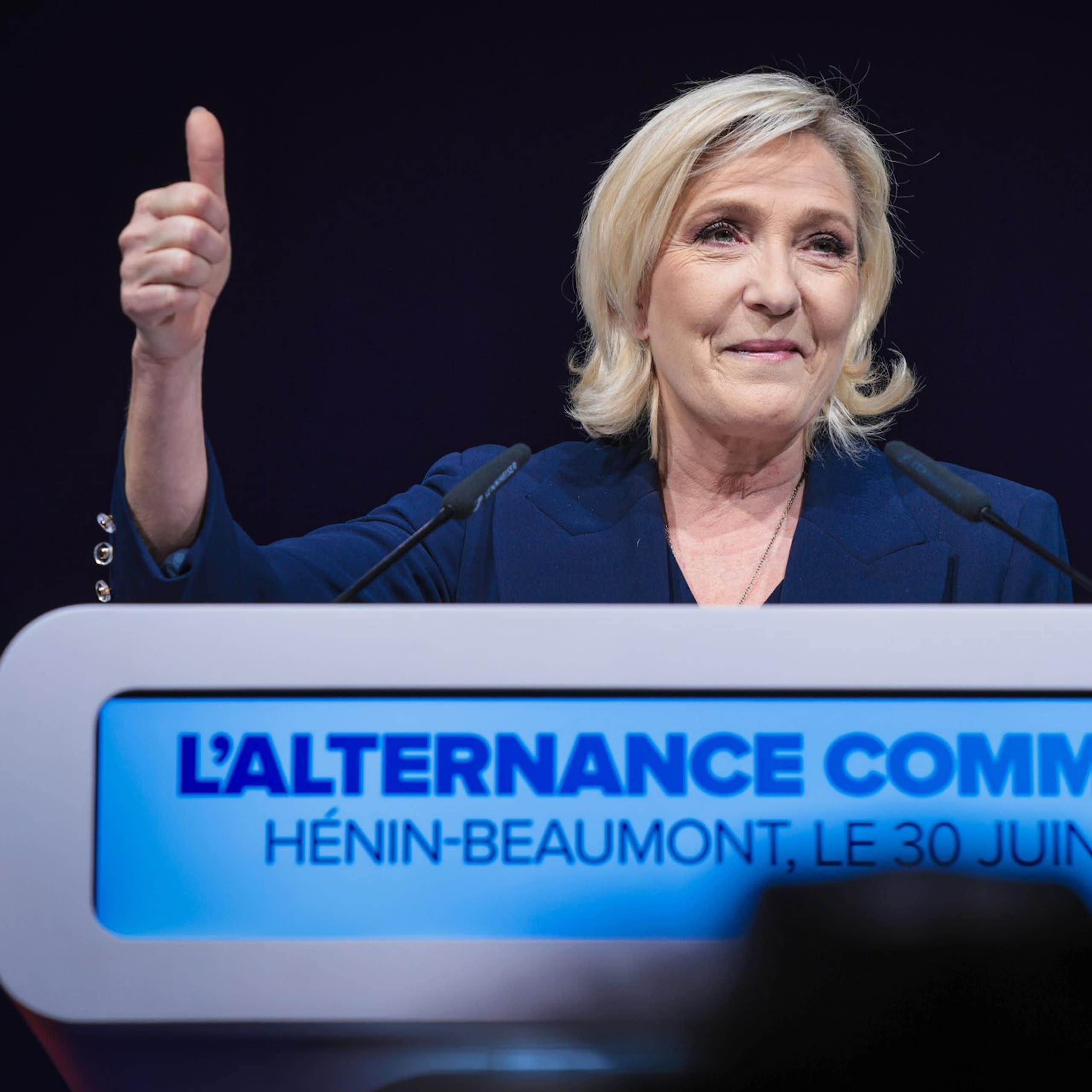 Marine Le Pen smirking and holding her thumb up in the air.