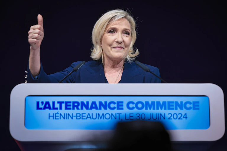 Marine Le Pen smirking and holding her thumb up in the air.