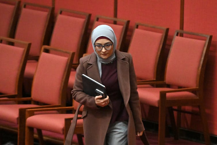 A woman holds a notebook as she walks through rows of red seats.