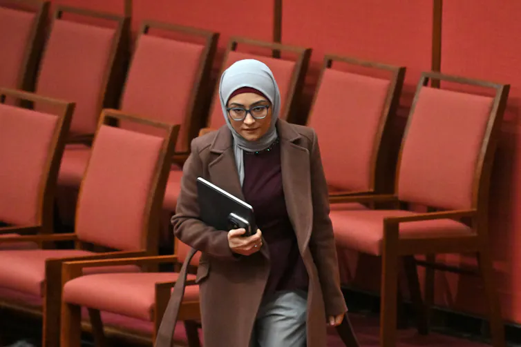A woman holds a notebook as she walks through rows of red seats.