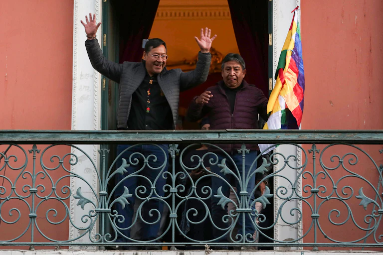 Luis Arce and his vice president standing on a balcony greeting supporters.