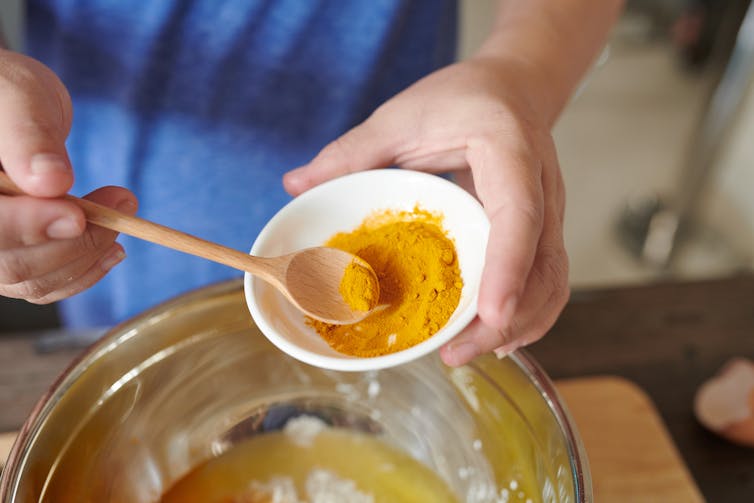A person spoons turmeric into a mixing bowl.