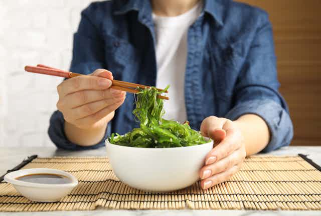A person uses chopsticks to pick up Japanese seaweed from a bowl.