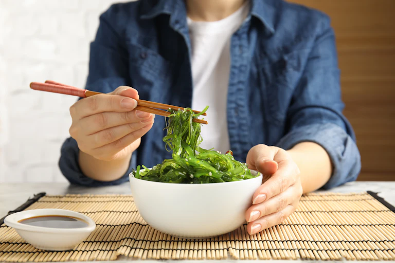 A person uses chopsticks to pick up Japanese seaweed from a bowl.