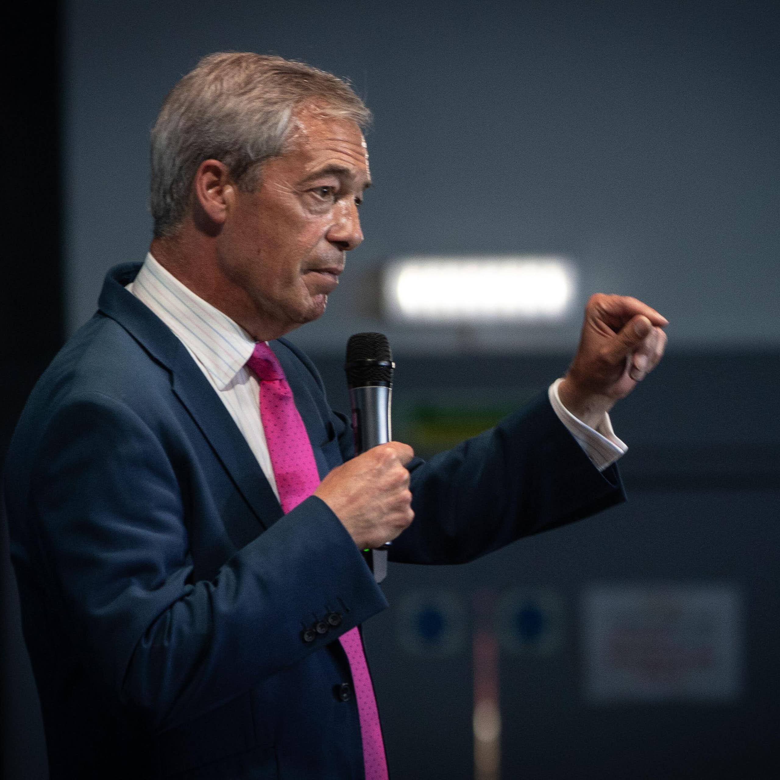 Side view of Nigel Farage holding a microphone and gesturing with his other hand