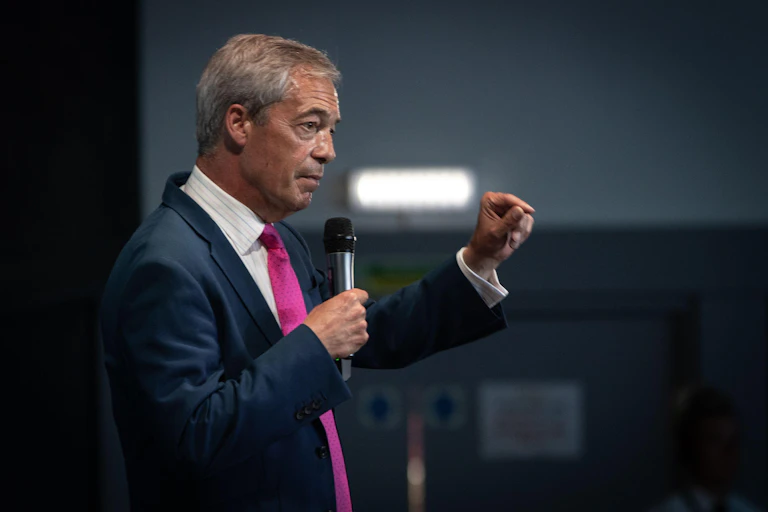 Side view of Nigel Farage holding a microphone and gesturing with his other hand