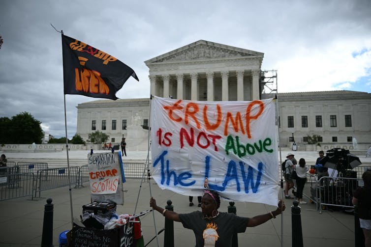 People stand outside the Supreme Court and hold signs, one of which that says, 'Trump is not above the law'