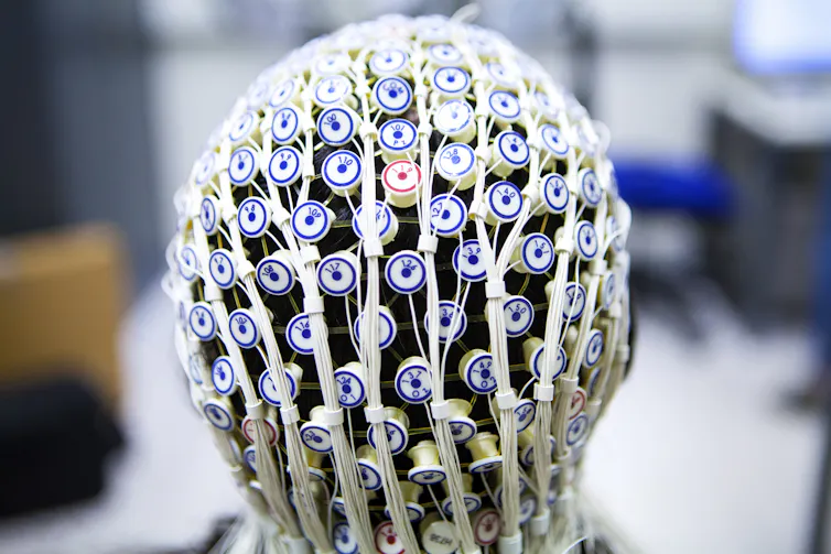 Parte de trás da cabeça de uma pessoa envolvida pelos muitos e pequenos eletrodos redondos de uma touca de EEG