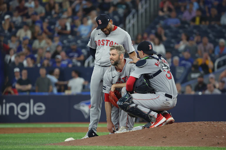 Player in baseball uniform sans hat kneels on the mound while a player in catching equipment kneels next to him and rests his hand on his shoulder.