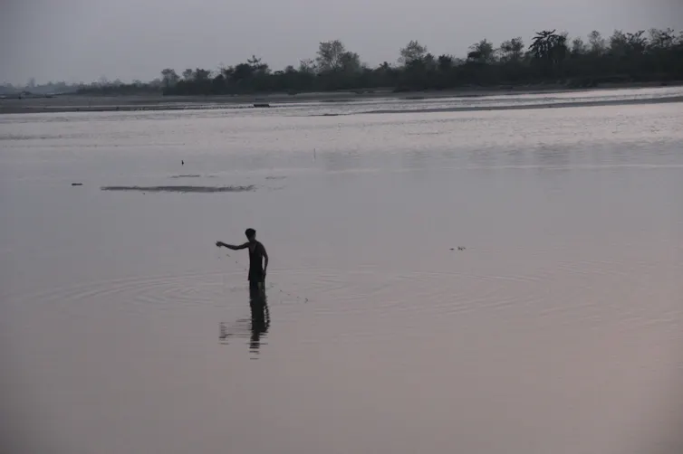 A man stands in a low river with a fishing net in his hand.