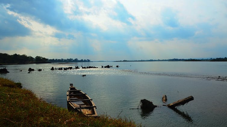 A view of a wide river with a small hand-made boat on the shore.
