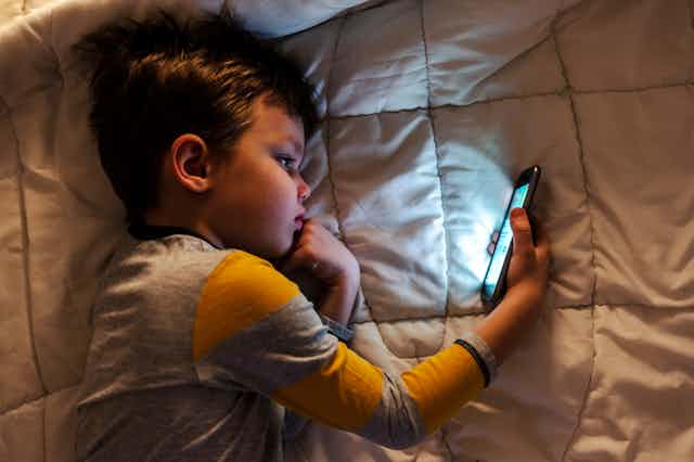 A young child lying on a blanket looking at a smartphone screen.