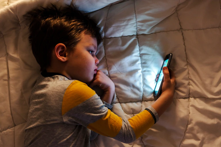 A young child lying on a blanket looking at a smartphone screen.