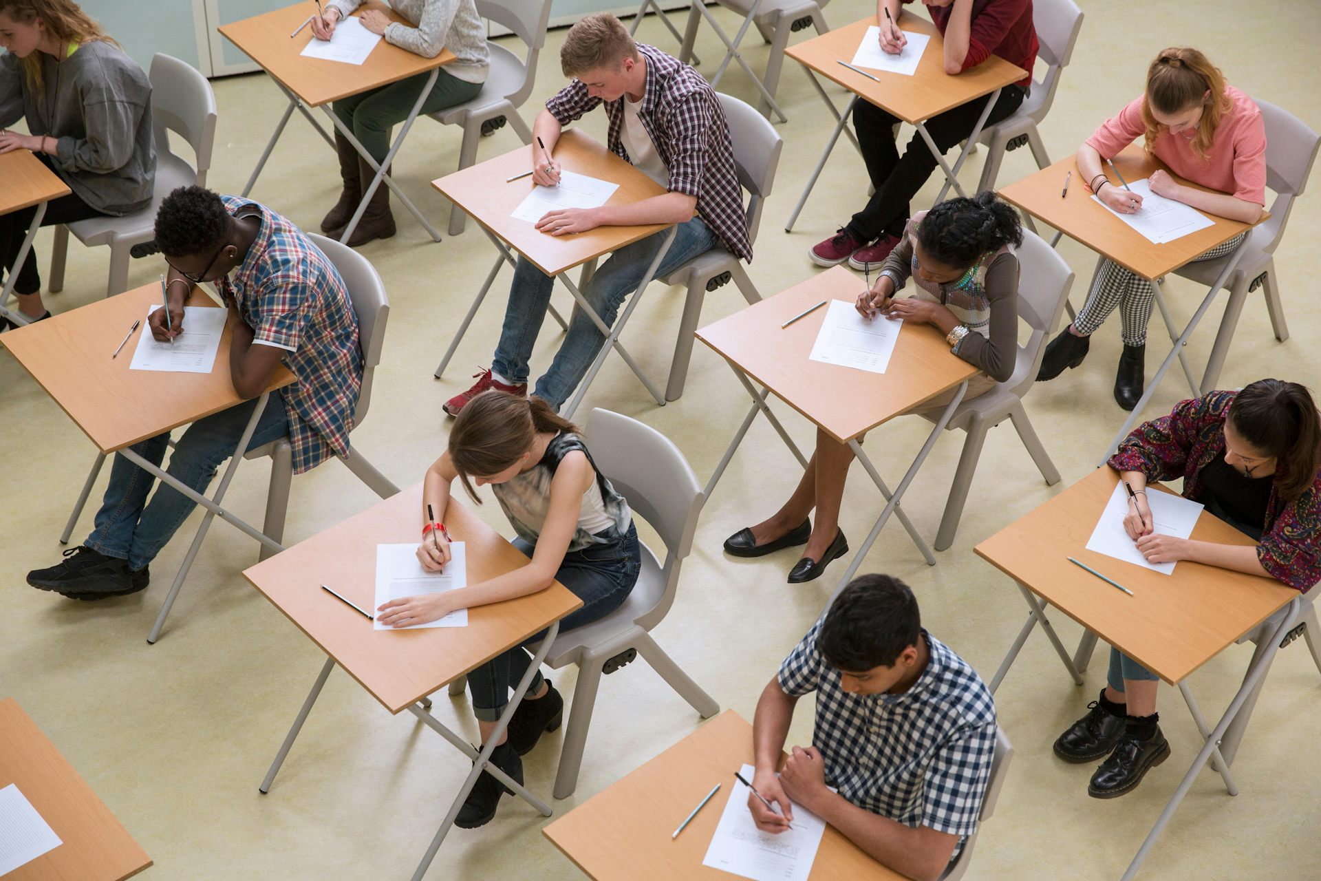 Jovens sentados em carteiras escolares fazendo provas.
