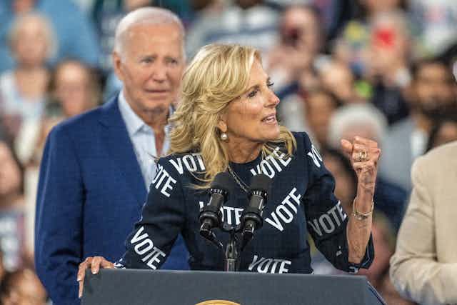 Jill Biden clenches her fist as she speaks to a crowd. Behind her is her huband, US president Joe Biden.