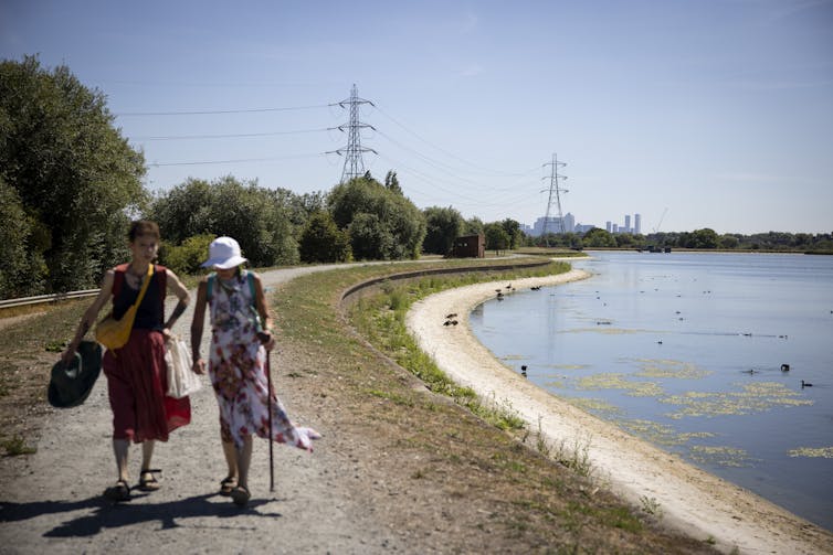 Two people walk alongside a reservoir at low level.
