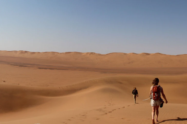 Two people walking in a landscape of sand dunes