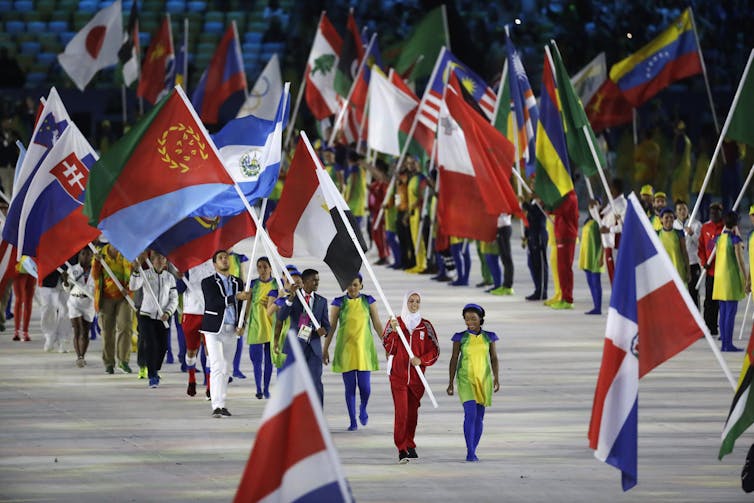 People dressed colorfully walk in rows while holding flags.