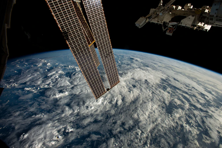 long thin rectangular structure in orbit above clouds on Earth
