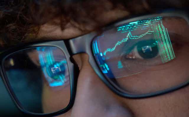Person looking at trading charts reflecting in glasses, close up