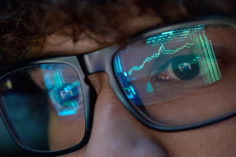 Person looking at trading charts reflecting in glasses, close up