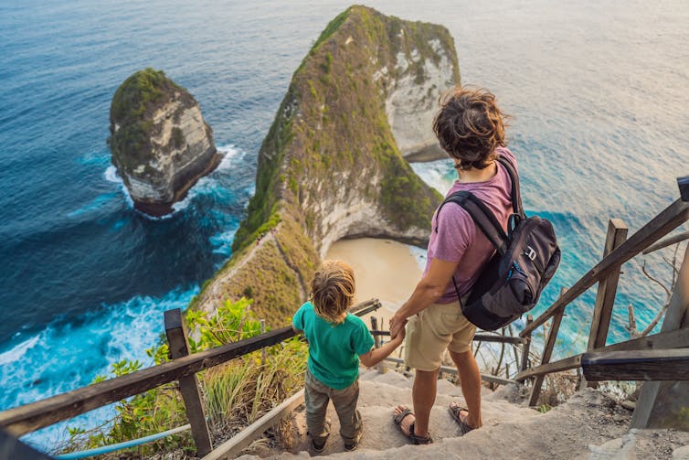 A man and boy looking down on a cliff and beach in Bali.