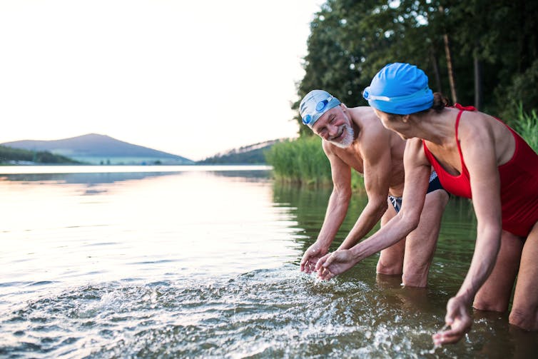 A elderly couple wearing goggles and swimming caps get ready to go wild swimming.