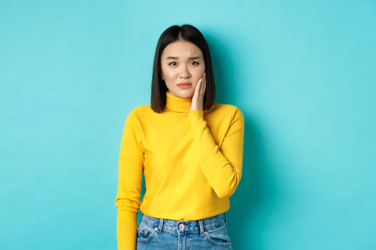 Asian young woman touching cheek and frowning, looking sad, being slapped in face