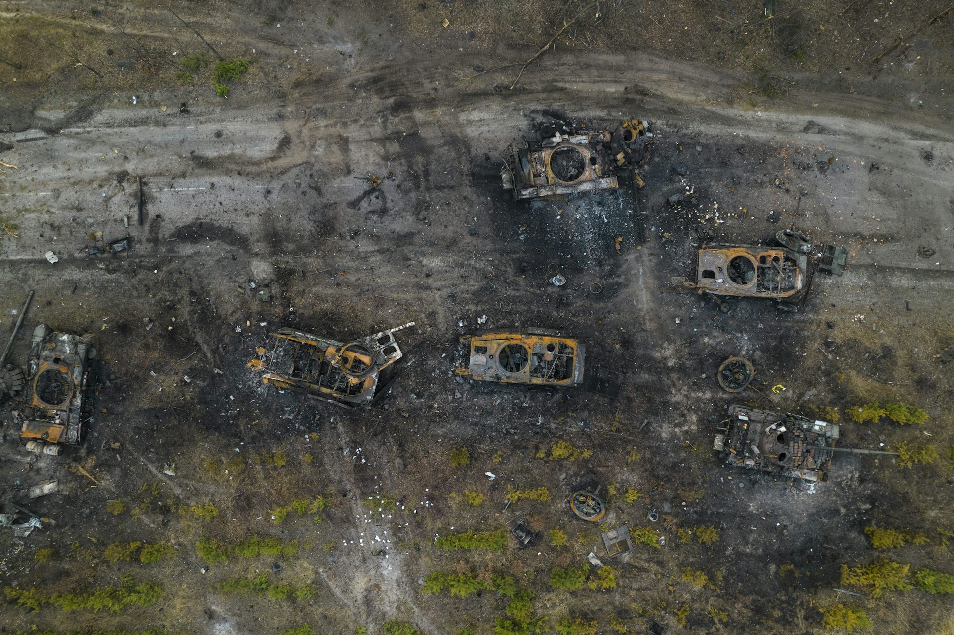An aerial view of destroyed tanks on soot-covered ground.
