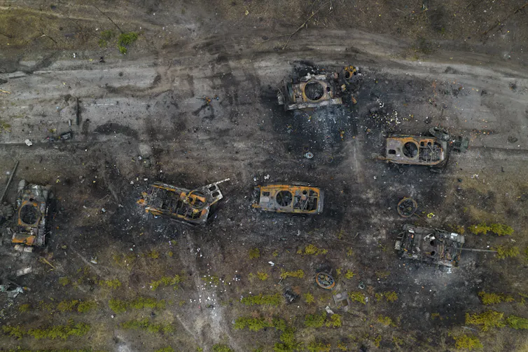 An aerial view of destroyed tanks on soot-covered ground.