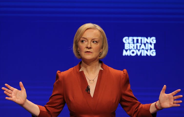 Liz Truss ao lado de uma placa com os dizeres