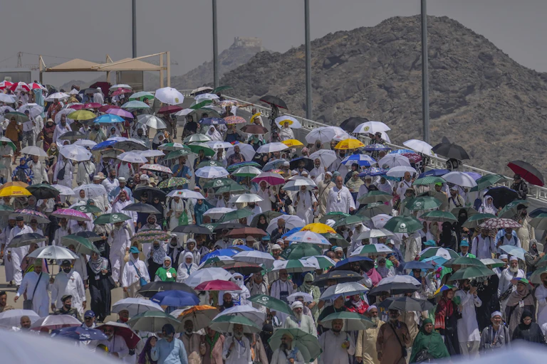 A large number of people holding umbrellas to shield themselves from the sun, with a bare mountain range in the background.