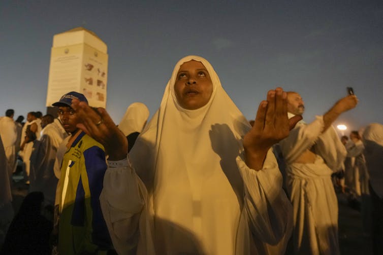A woman with her head and neck covered holds up her hands as she looks toward the sky.