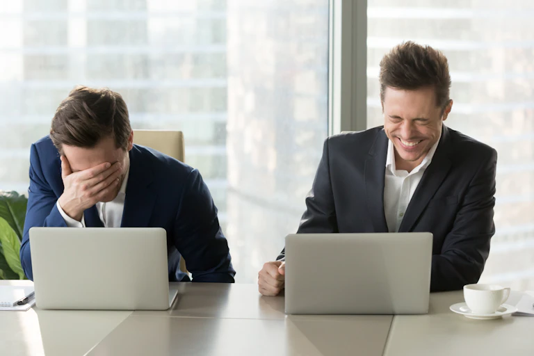 Deux hommes assis devant des ordinateurs rient.