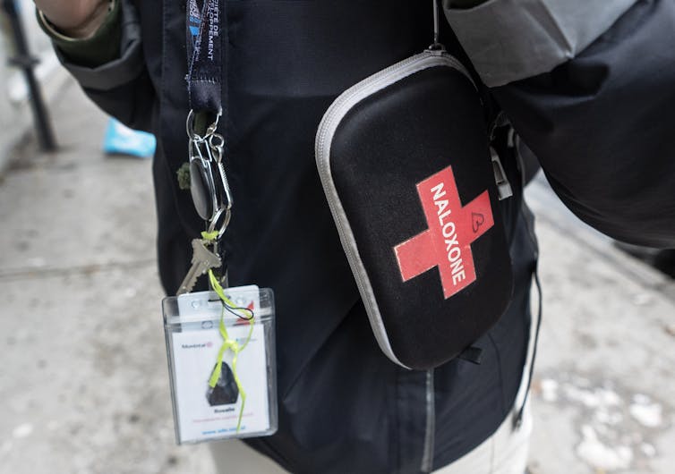 Close-up of a black naloxone kit with a red cross and smudged ID tag on the lanyard.