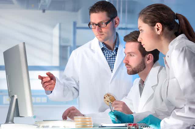 Two men and a woman in white coats look an a monitor