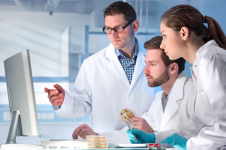 Two men and a woman in white coats look an a monitor