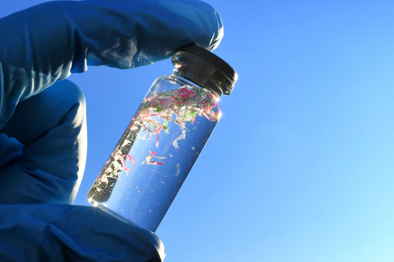 a gloved hand holds a vial of water with tiny plastic pieces floating in it