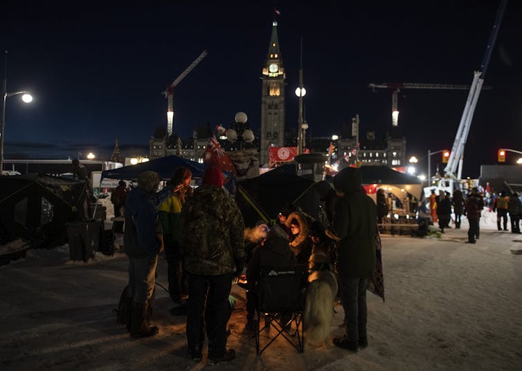 a group of people huddled around a fire at night, police in the background