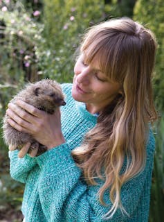 woman with green jumper and long hair holding small hedgehog in her hands