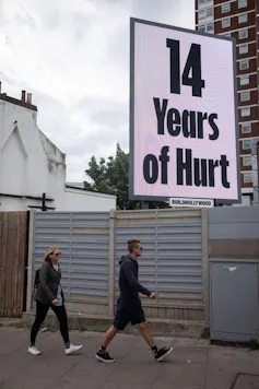A poster reading '14 years of hurt' with two people walking past.